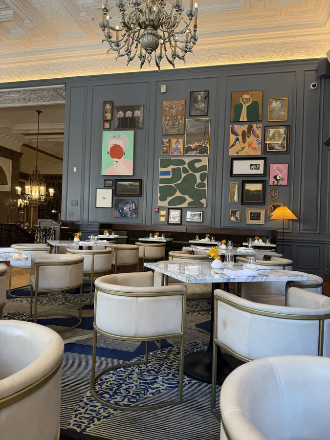 A quiet restaurant dining room, marble tables and a wall of framed prints under low lamplight.
