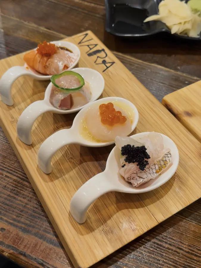 Four ceramic tasting spoons on a wooden board, each with a different garnished bite.